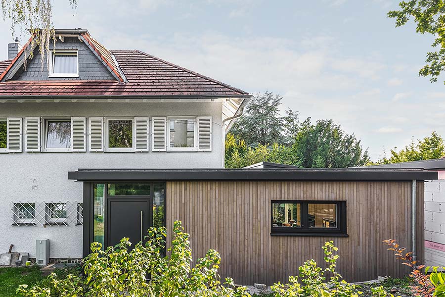 Nachhaltiger Anbau an ein Wohnhaus mit horizontaler Holzfassade und Eingangstür